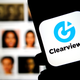 Clearview AI company logo on the smartphone screen held in hands with blurred faces in the background. Concept photo for face recognition software.